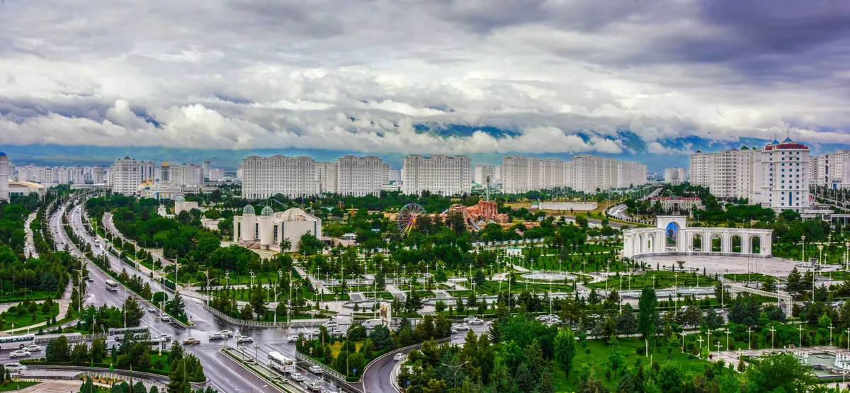 Panoramic view of Ashgabat, Turkmenistan with green parks, wide avenues, and white buildings under a dramatic cloudy sky