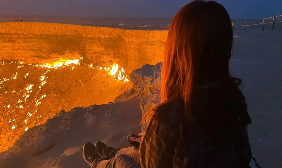 Traveler at the edge of the Darvaza Gas Crater at night, glowing flames in the Karakum Desert, Turkmenistan